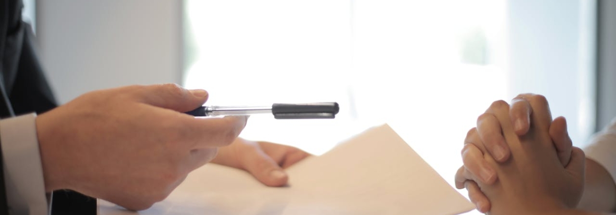 Person Handing Personal Loan Documents and Pen To Another Over a White Table