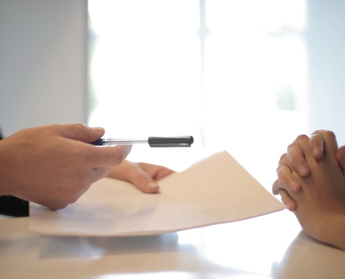 Person Handing Personal Loan Documents and Pen To Another Over a White Table